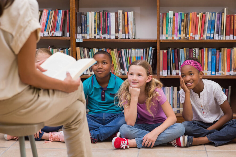 Cute pupils and teacher having class in library at the elementary school