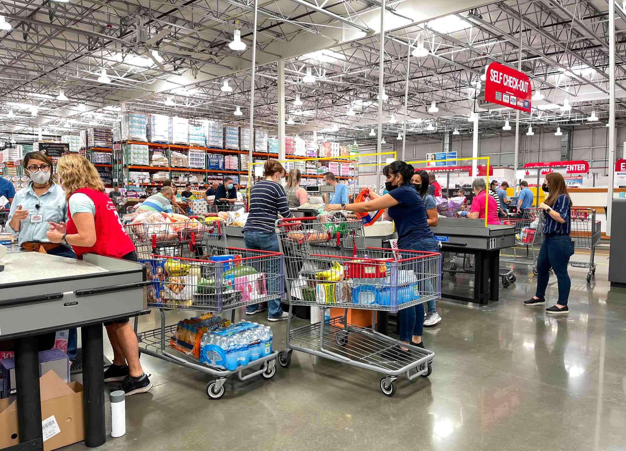 The check out counter at the Costco grocery store with employees checking out various customers.