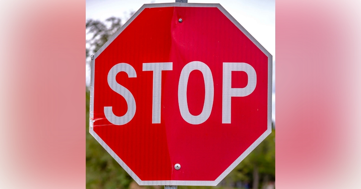 Red stop sign against trees and sky on a sunny day